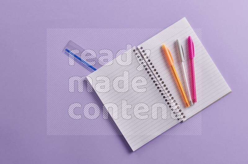 A blank open notebook with school supplies on purple background