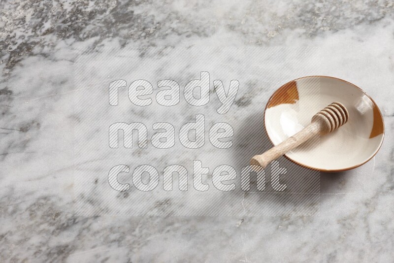 Multicolored pottery plate with wooden honey dipper in it on grey marble background