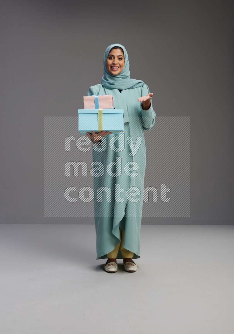 Saudi Woman wearing Abaya standing holding gift box on Gray background