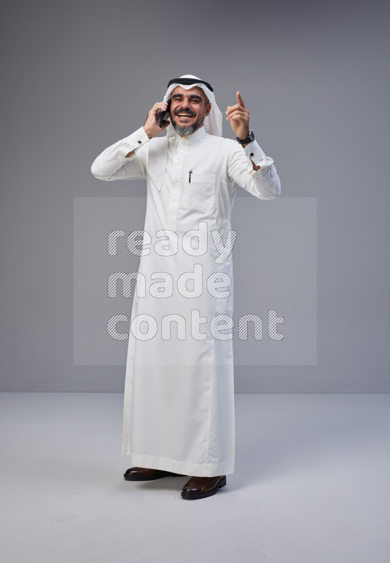 Saudi man Wearing Thob and white Shomag standing talking on phone on Gray background