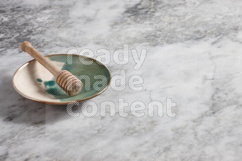 Multicolored pottery plate with wooden honey dipper in it on grey marble background