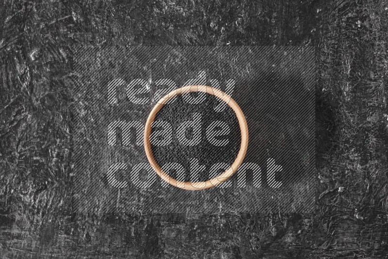 وعاء خشبي ممتلئ ببذور حبة البركة علي خلفية سوداء