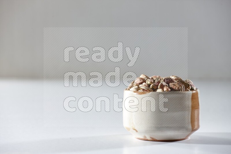 A beige ceramic bowl full of peeled pistachios on a white background in different angles