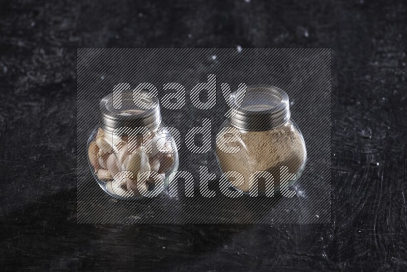 2 glass spice jars full of garlic powder and cloves on a textured black flooring