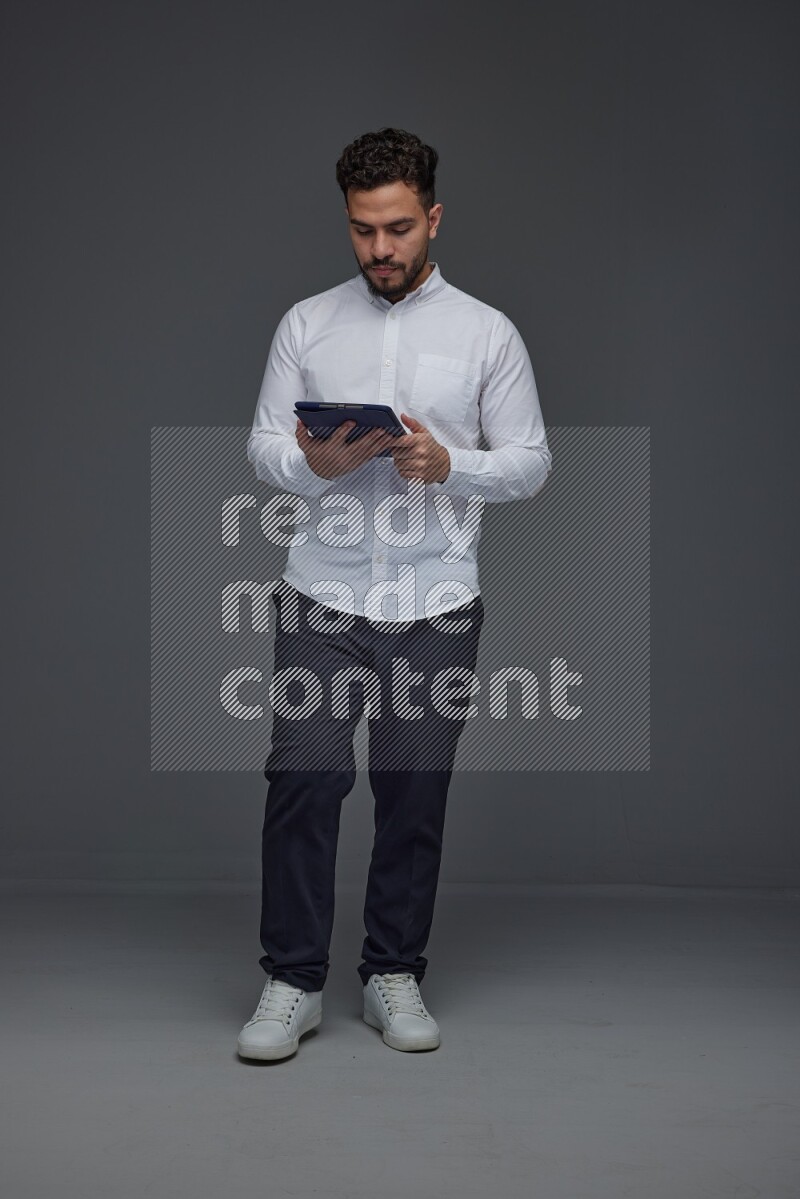A man wearing smart casual standing and using his tablet eye level on a gray background