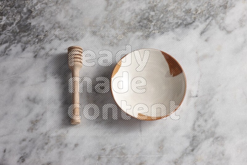 Multicolored pottery plate with wooden honey dipper on the side on grey marble background