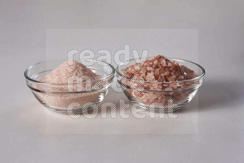 2 glass bowls one is filled with fine himalayan salt and the other with coarse himalayan salt on white background