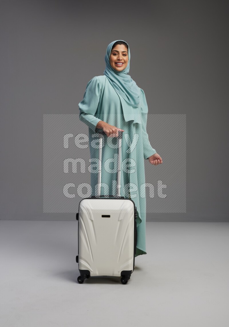 Saudi Woman wearing Abaya standing holding Travel bag on Gray background