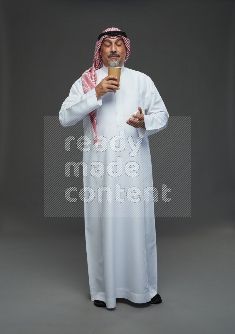 Saudi man with shomag Standing holding paper cup on gray background