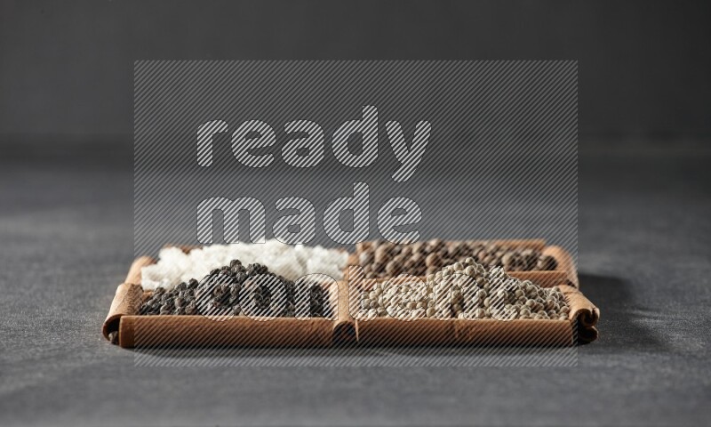 4 مربعات من عيدان القرفة ممتلئة بحبوب الفلفل الأسود والفلفل الأبيض وبهار الفلفل الحلو والملح الأبيض على أرضية سوداء