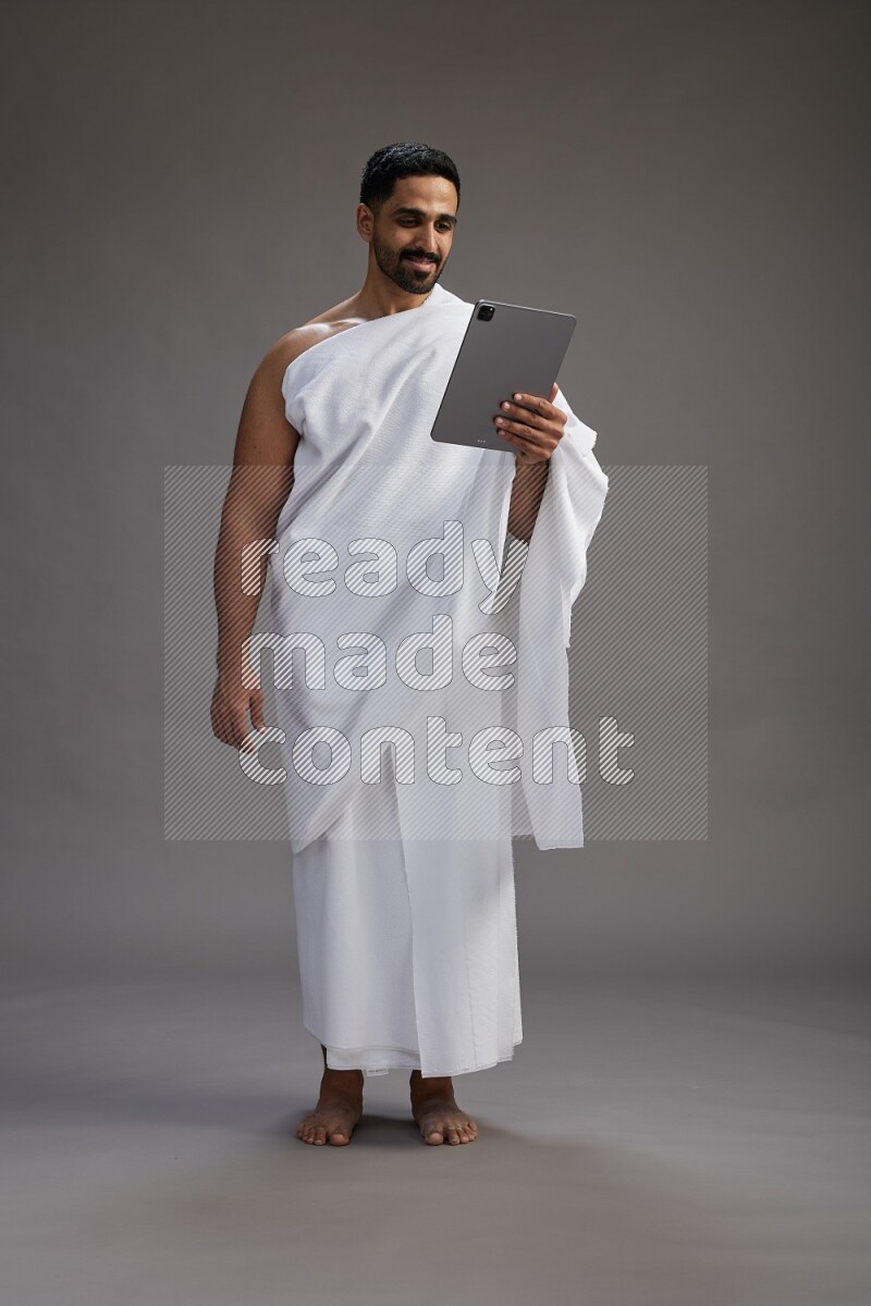 A man wearing Ehram and holding a tablet on gray background