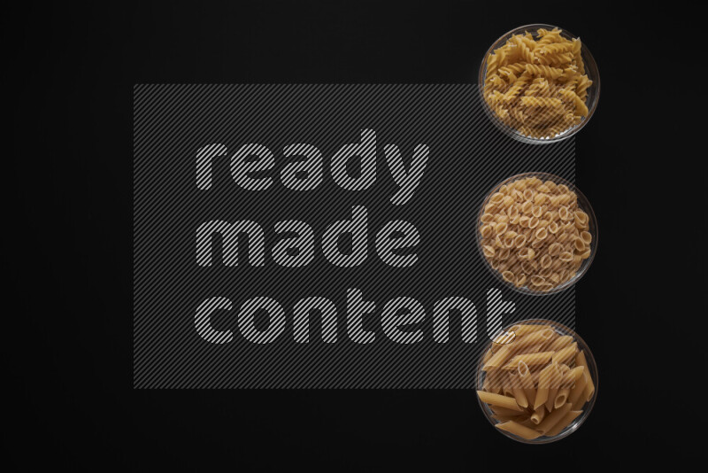 Different pasta types in 3 glass bowls on black background