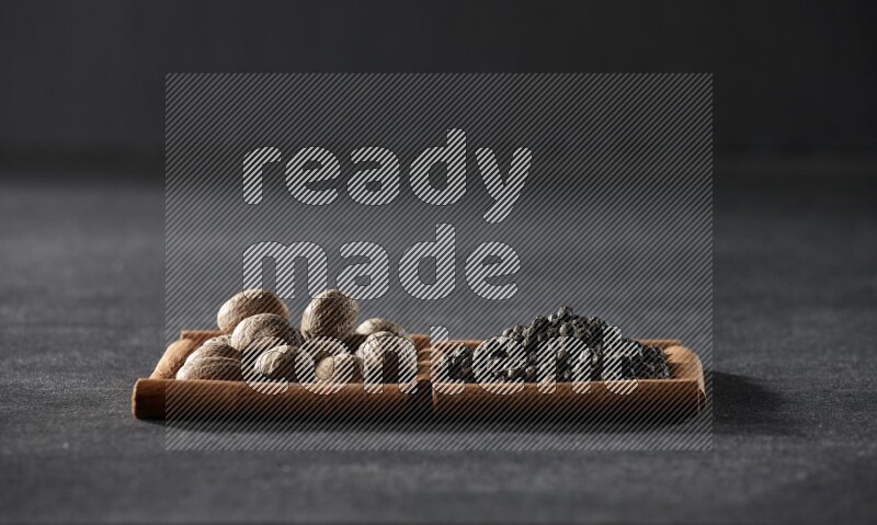 2 squares of cinnamon sticks full of nutmegs and black peppers on black flooring