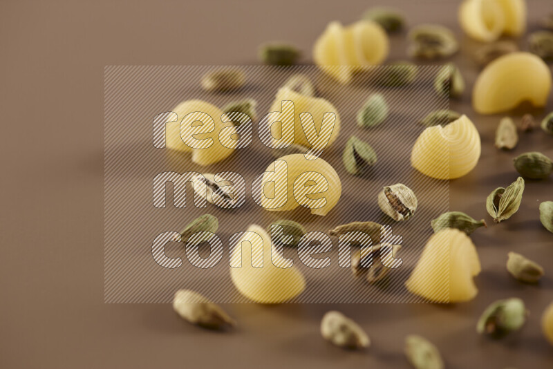 Raw pasta with different ingredients such as cherry tomatoes, garlic, onions, red chilis, black pepper, white pepper, bay laurel leaves, rosemary and cardamom on beige background