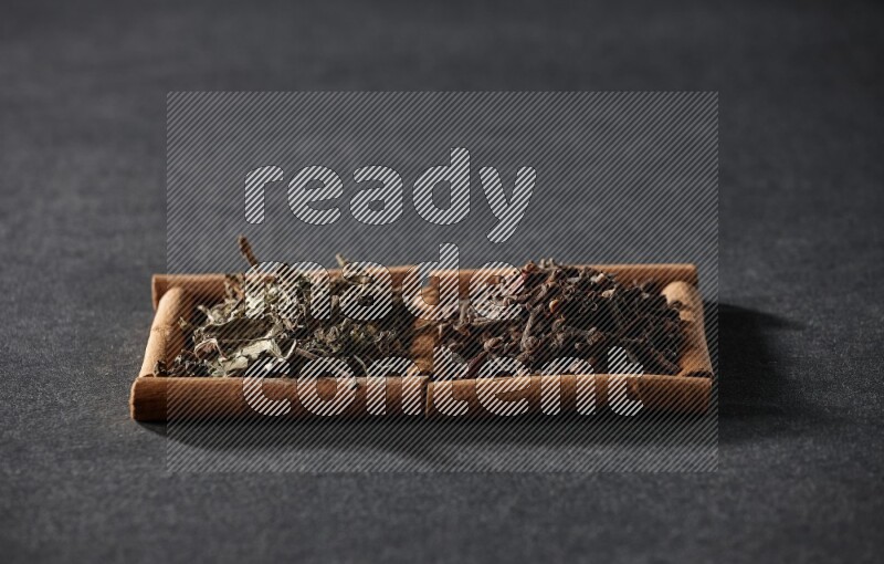 مربعان من أعواد القرفة ممتلئان بالقرنفل والريحان المجفف علي خلفية سوداء