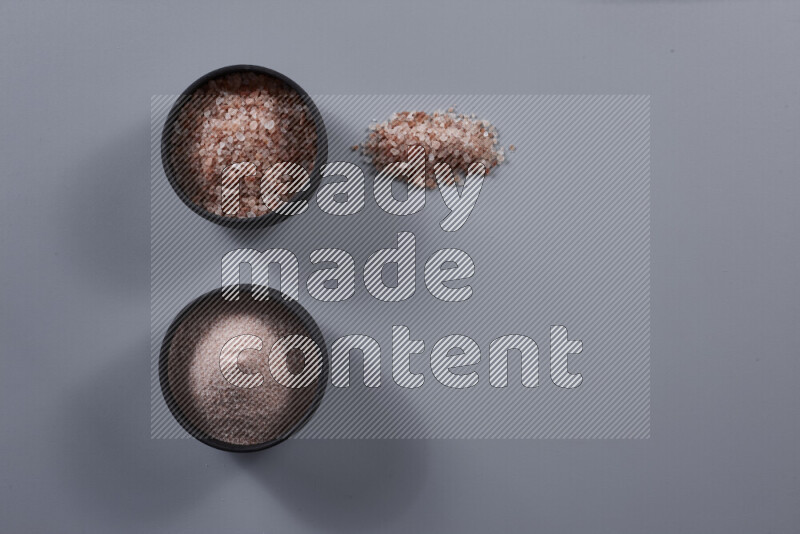 2 pottery bowls one is filled with fine himalayan salt and the other with coarse himalayan salt on grey background