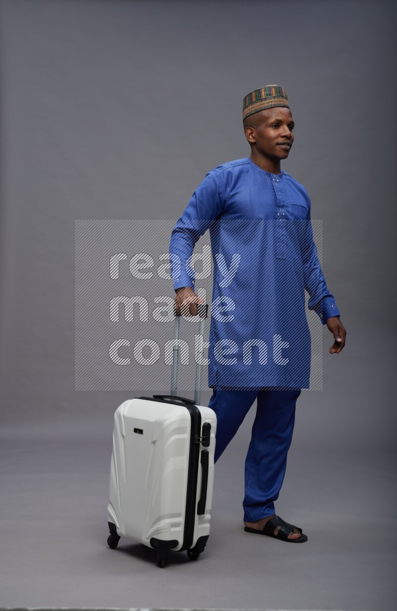 Man wearing Nigerian outfit standing holding bag on gray background
