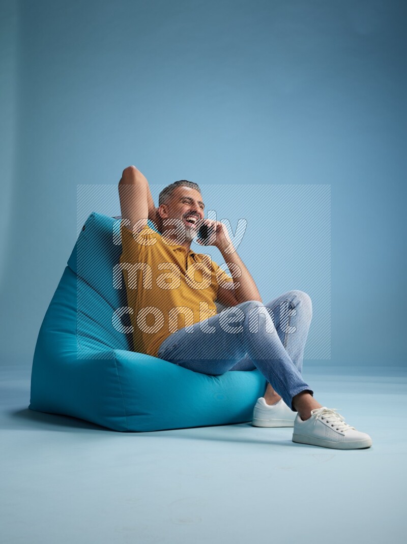 A man sitting on a blue beanbag and talking on the phone