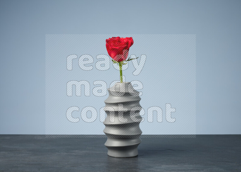 An arrangement of vivid red roses in a grey spiral vase on black marble background