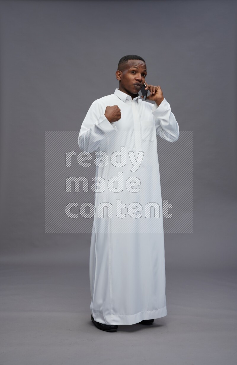 Saudi man wearing thob standing talking on phone on gray background