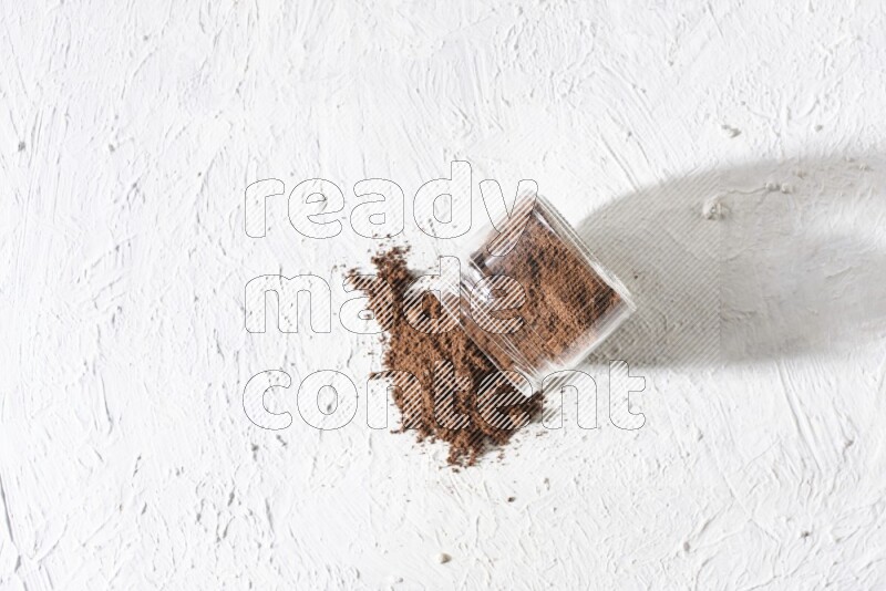 A flipped glass jar full of cloves powder on a textured white flooring