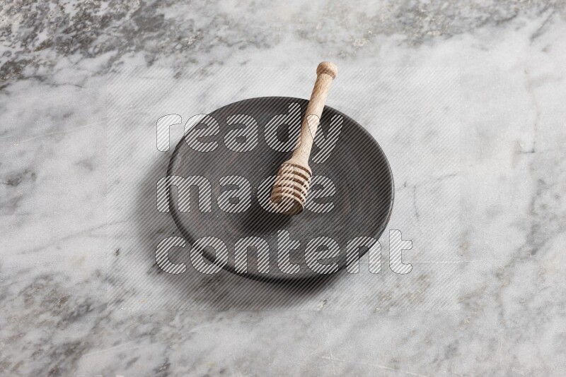 Black pottery plate with wooden honey dipper in it on grey marble background