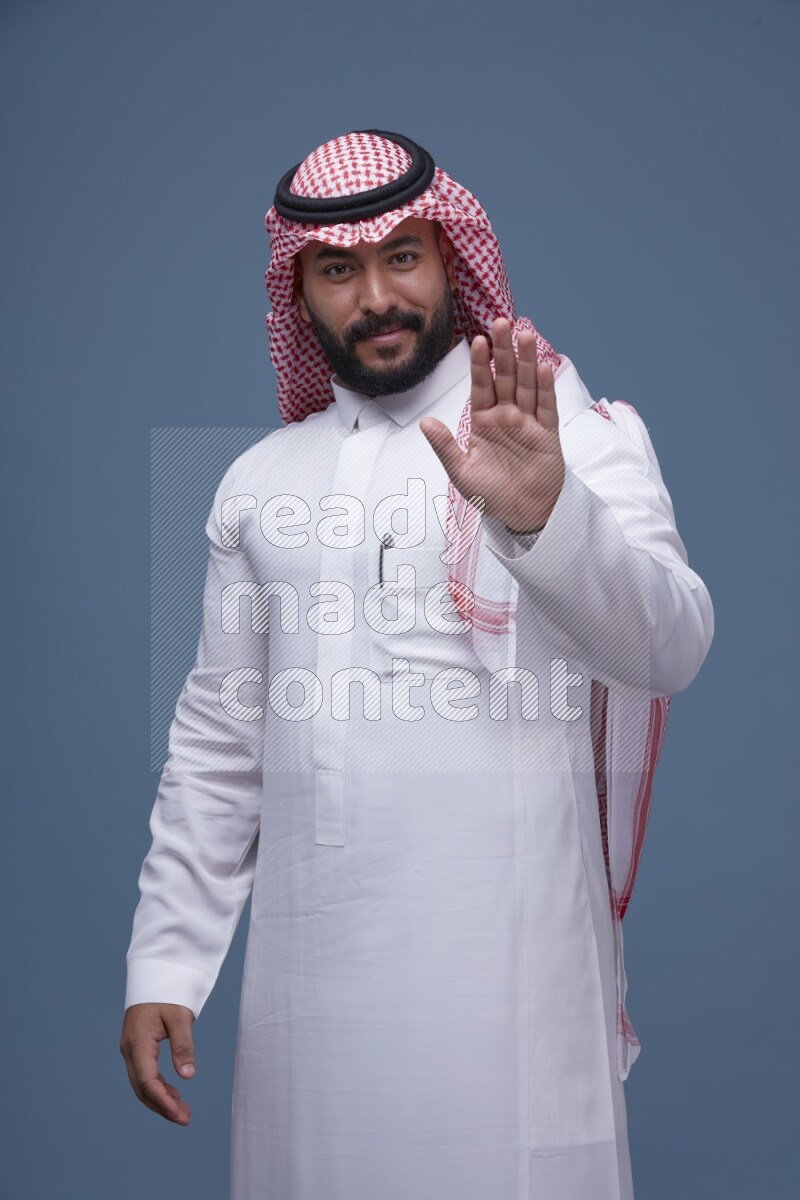 A Saudi man posing on blue background wearing Thob and Shomag