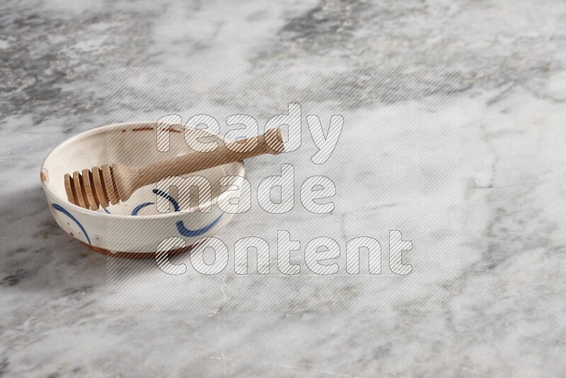 Multicolored pottery bowl with wooden honey dipper in it on grey marble background
