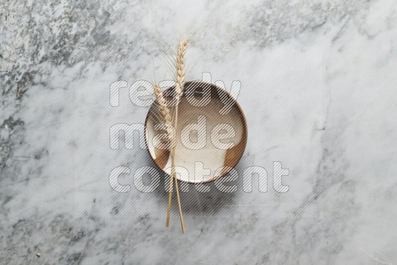 Wheat stalks on multicolored pottery plate on grey marble background