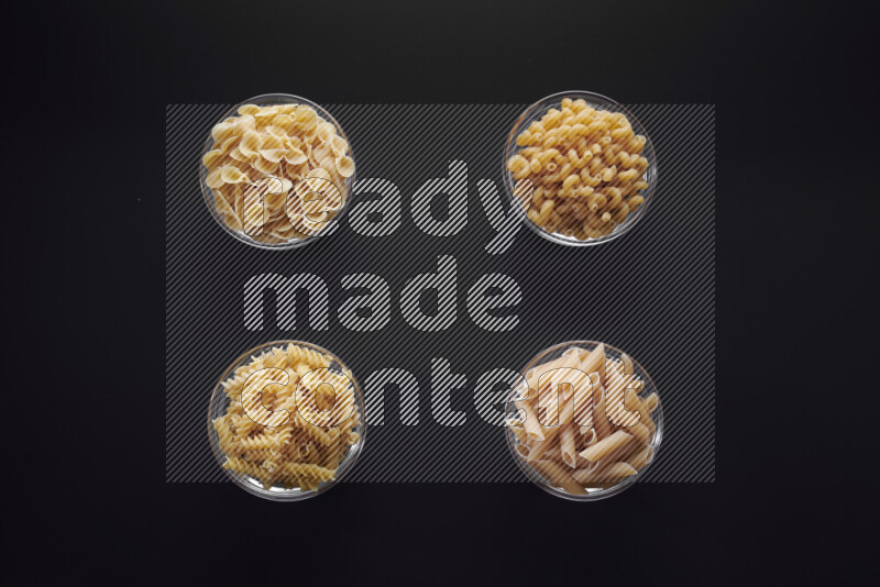 Different pasta types in glass bowls on black background