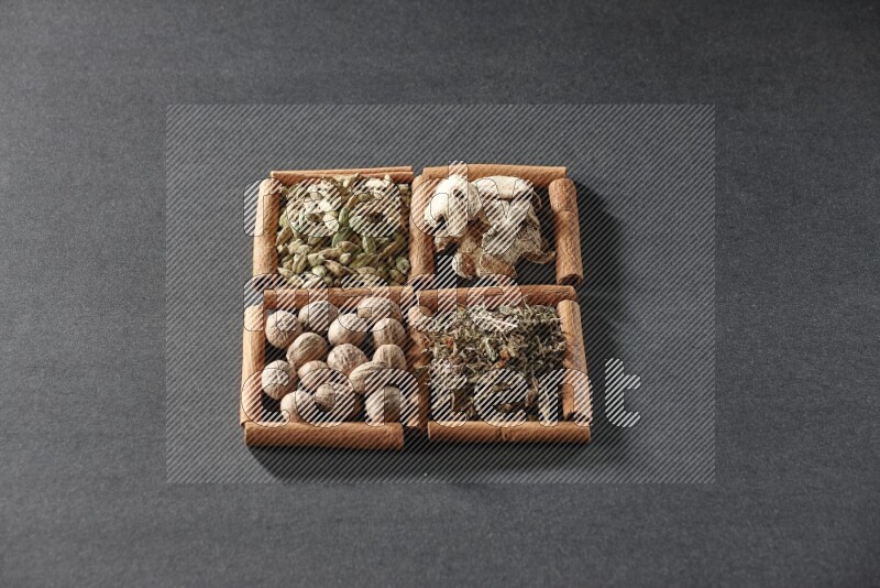 4 مربعات من عيدان القرفة ممتلئة بالريحان المجفف والهيل والزنجبيل المجفف وجوزة الطيب على أرضية سوداء