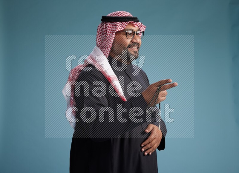 Saudi Man with shimag Standing Interacting with the camera on blue background