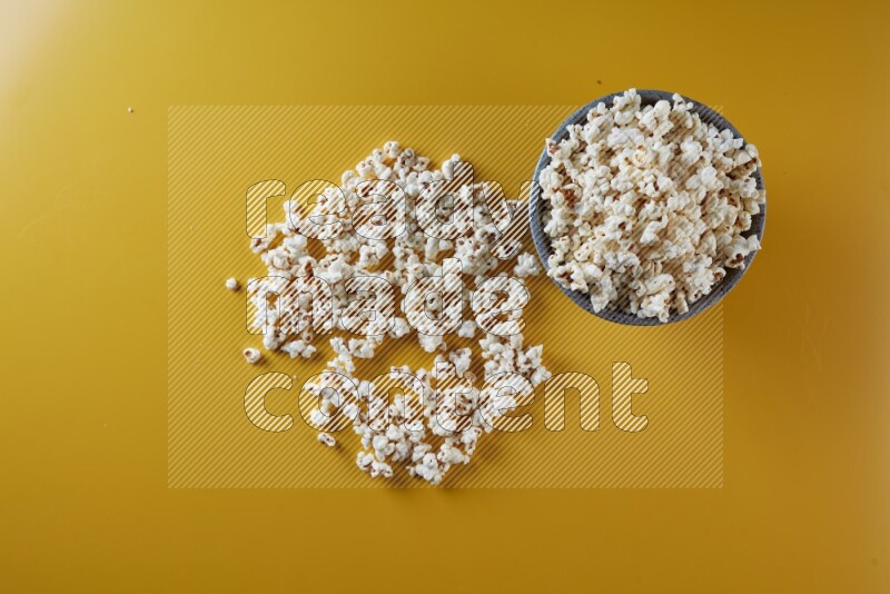 A multicolored pottery bowl full of popcorn with popcorn beside it on a yellow background in different angles