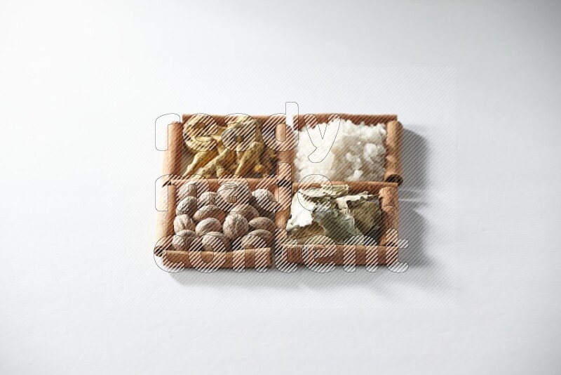 4 مربعات من أعواد القرفة ممتلئة بالملح وورق الغار وجوزة الطيب والكركم على أرضية بيضاء