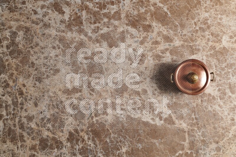 A small copper pot on beige marble background