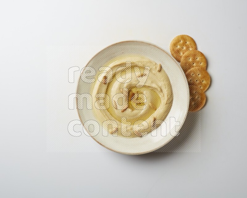 Hummus in a pottry plate garnished with pine nuts on a white background