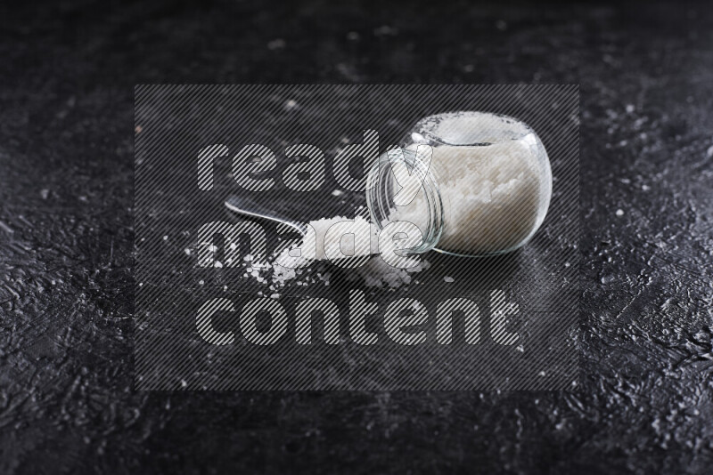 A glass jar full of coarse sea salt crystals on black background