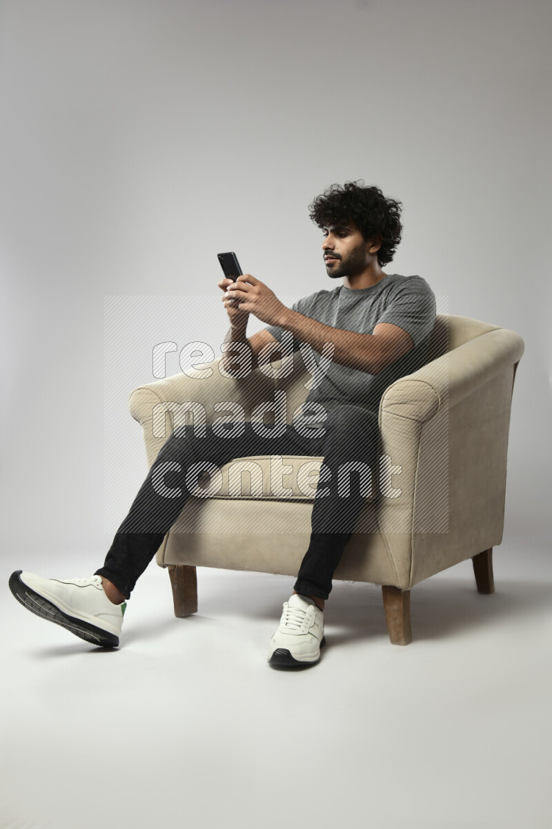 A man wearing casual sitting on a chair texting on the phone on white background