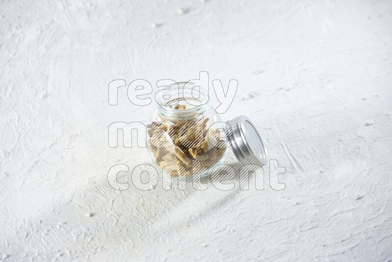 A glass spice jar full of dried turmeric whole fingers on a textured white flooring