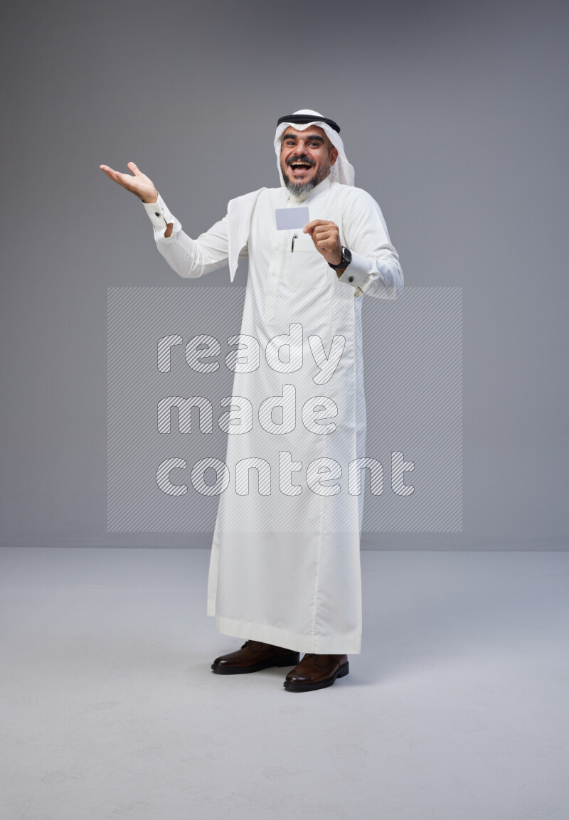 Saudi man Wearing Thob and white Shomag standing holding ATM card on Gray background