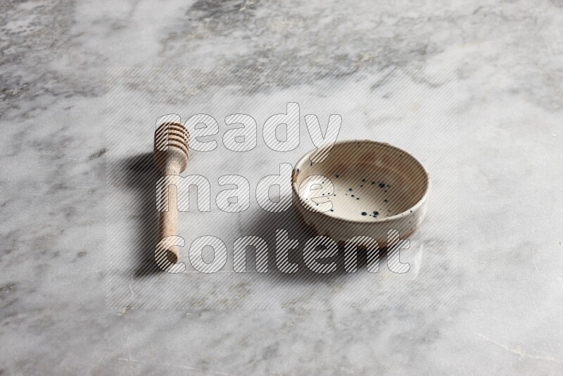 Multicolored pottery bowl with wooden honey dipper on the side on grey marble background