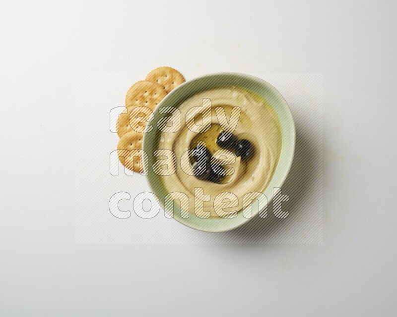 Hummus in a green plate garnished with black olives on a white background