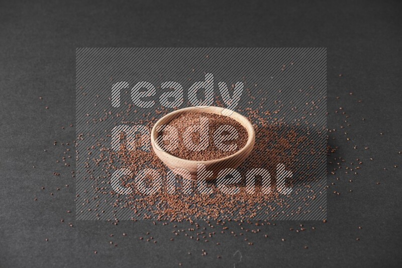 A wooden bowl full of garden cress seeds surrounded by seeds on a black flooring