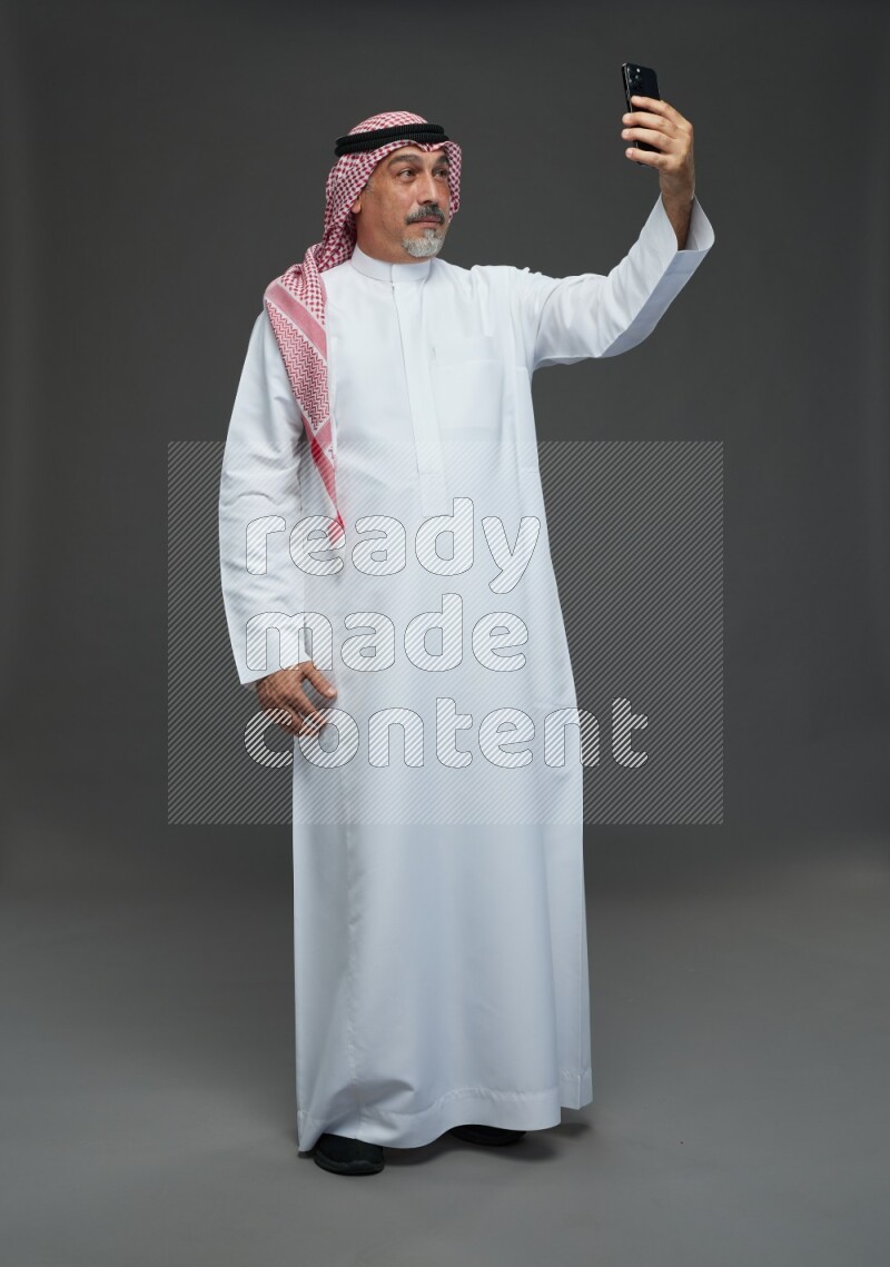 Saudi man with shomag Standing taking selfie on gray background