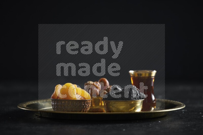Dried fruits in metal bowls on a tray in a dark setup