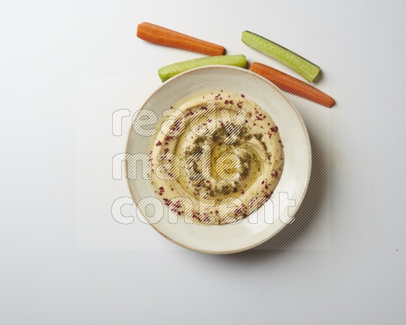 Hummus in a pottry plate garnished with zaatr & sumak on a white background