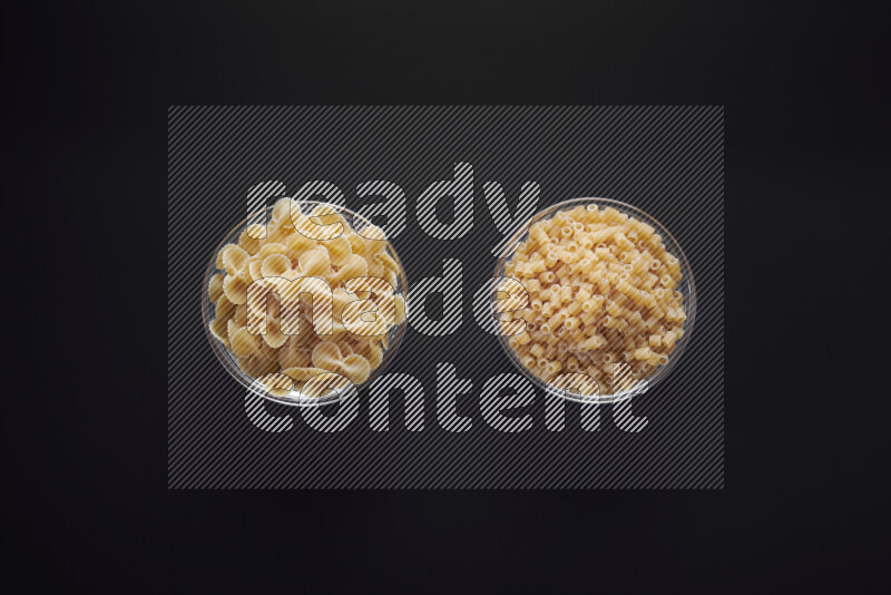 Different pasta types in glass bowls on black background