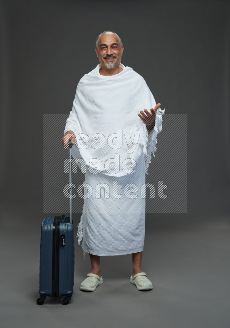 A man wearing Ehram Standing holding traveling bag on gray background