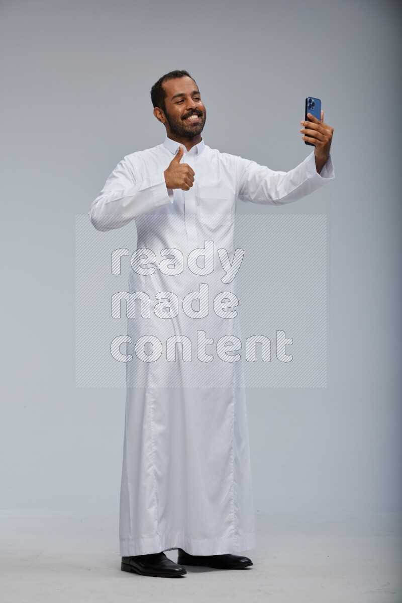 Saudi man wearing Thob standing taking selfie on Gray background