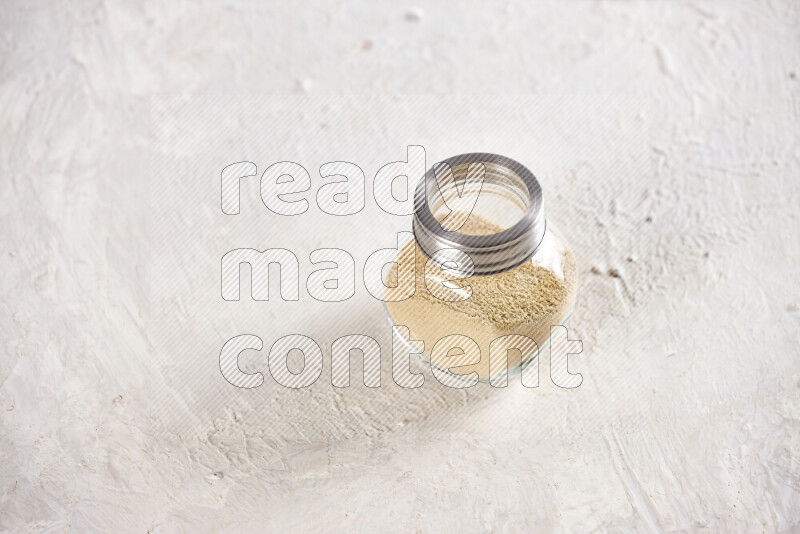 A glass jar full of ground ginger powder on white background
